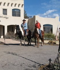 Two people are riding horses in front of a building.