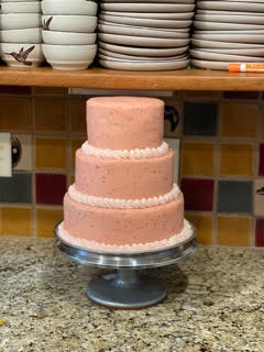 A pink cake is sitting on a cake stand on a counter.