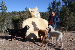 A man and three dogs are standing next to a statue of a cat.