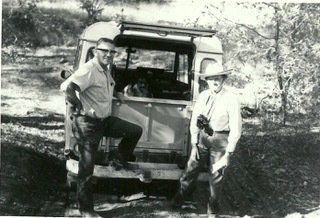 A black and white photo of two men standing next to a vehicle