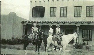 Three people are riding horses in front of a building.