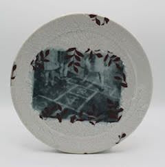 Ceramic plate with a central grayscale image of people playing hopscotch, encircled by a dark leaf pattern.