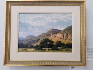 Landscape painting of mountains, trees, and cloudy sky in a gold frame.