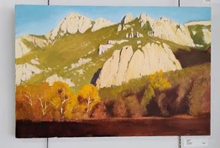 Mountains and autumn trees painting, light yellow rock formations, blue sky, and a dark brown foreground.