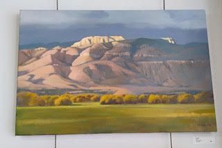 Landscape painting of a desert mountain under a cloudy sky, with yellow trees and a green field in the foreground.