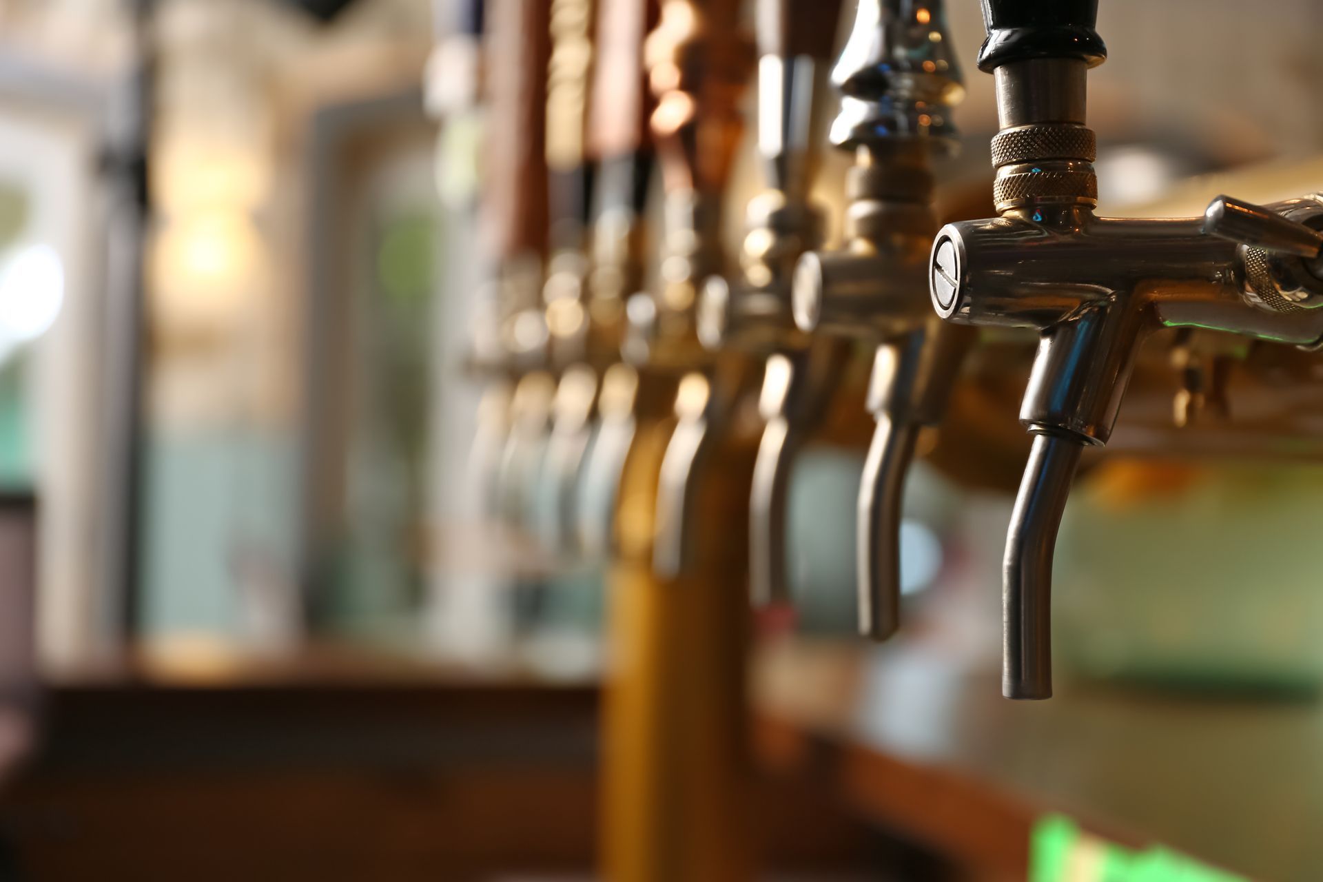 Row of beer taps at a bar, with metal faucets and warm blurred background