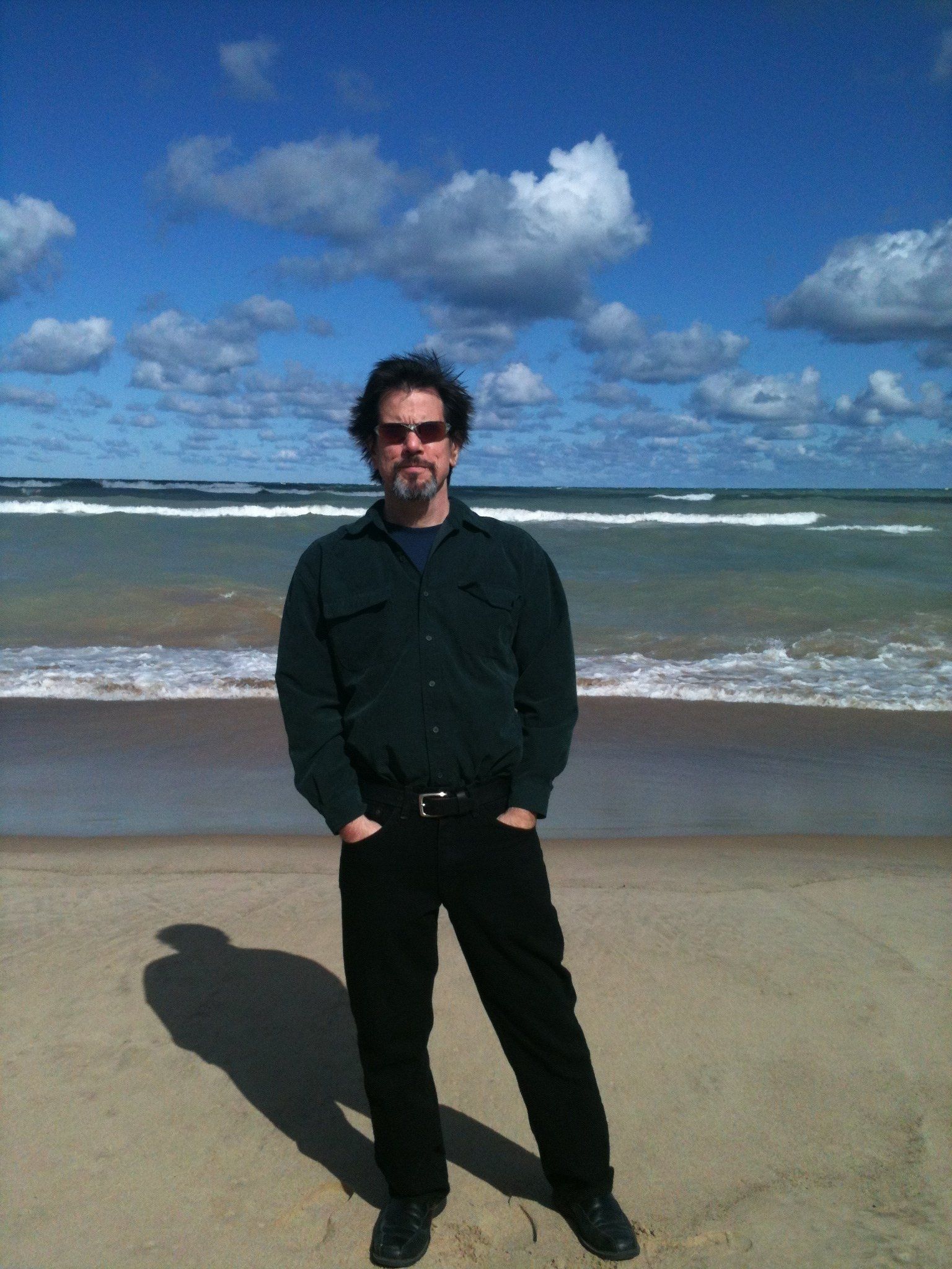 A man standing on a beach with his hands in his pockets