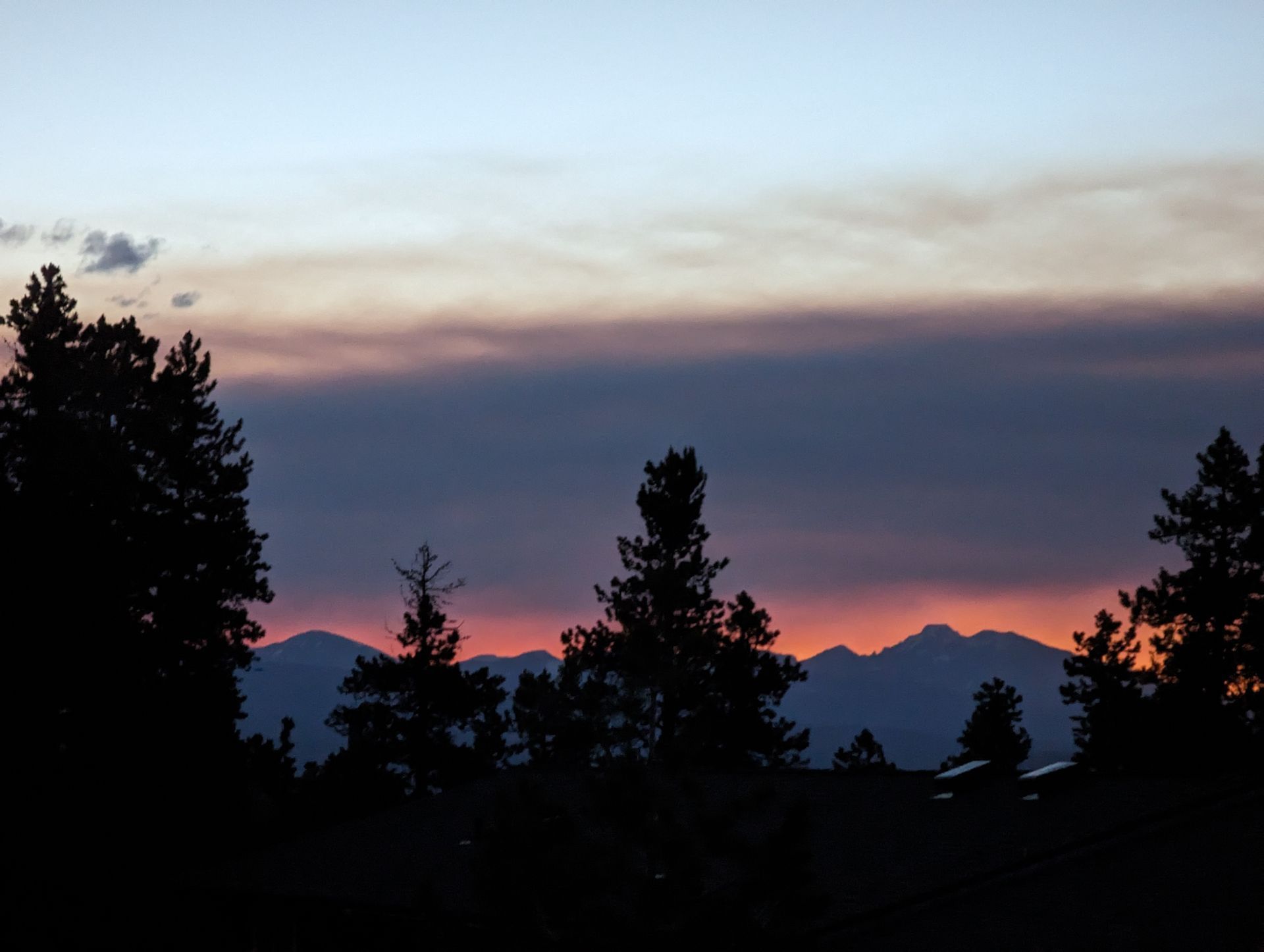 A sunset with trees in the foreground and mountains in the background