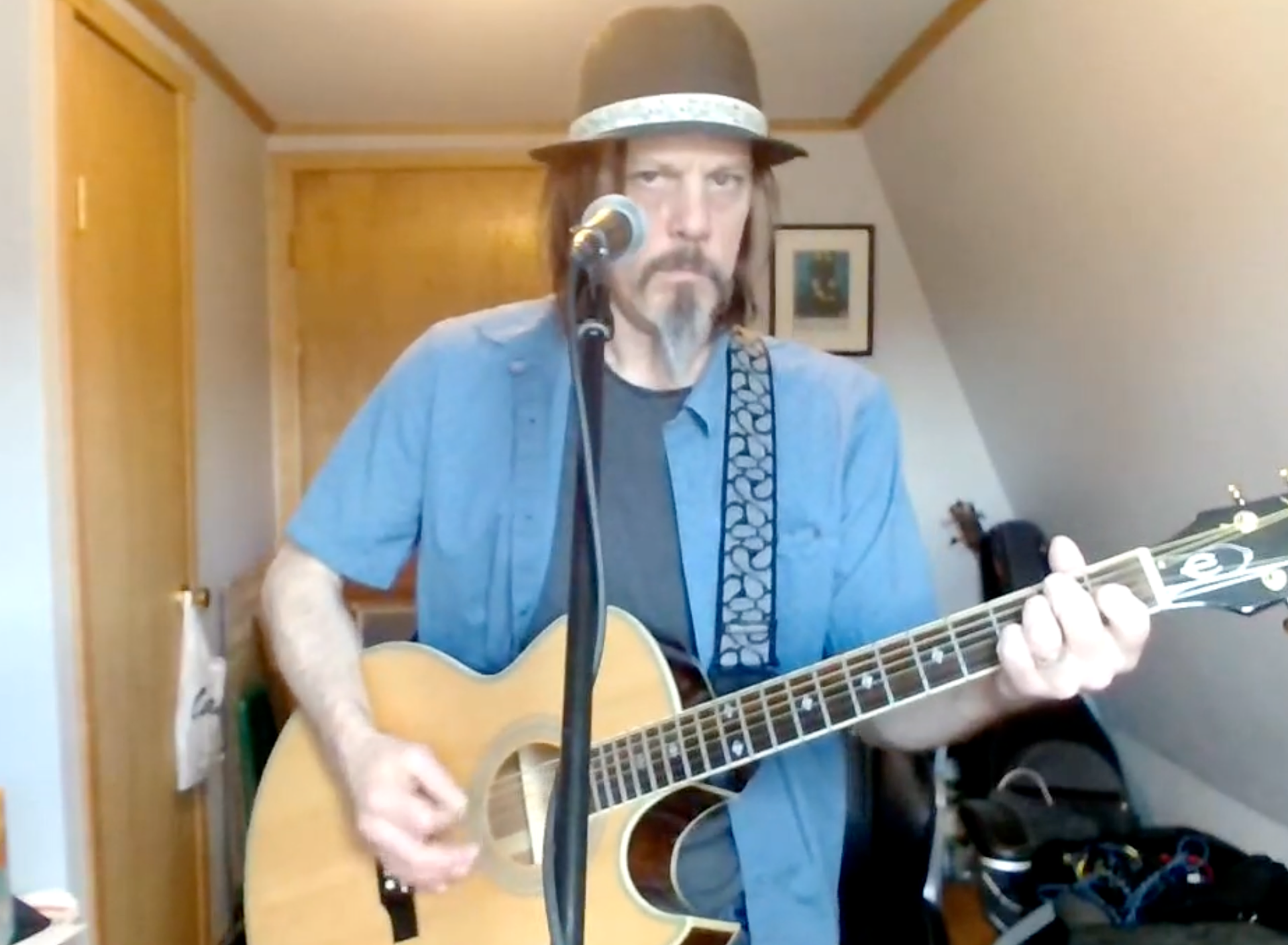 A man in a hat is singing into a microphone while playing a guitar