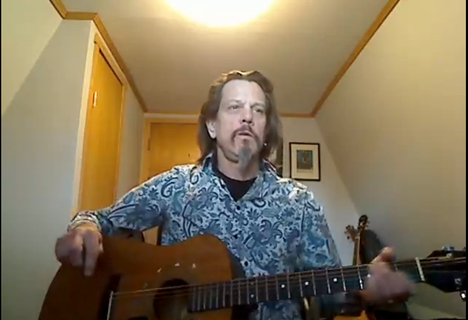 A man with a beard is playing an acoustic guitar in a room.