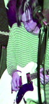 A man in a green and white striped shirt is playing a guitar in front of a microphone.