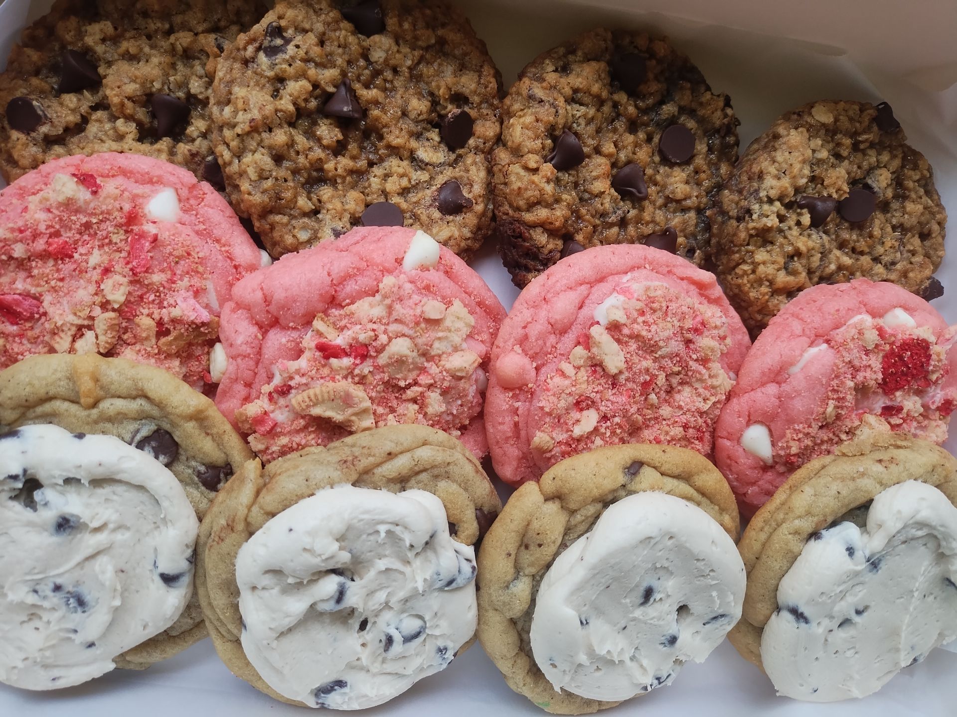 Assortment of cookies: chocolate chip, strawberry shortcake, and cookies with white icing, in a box.