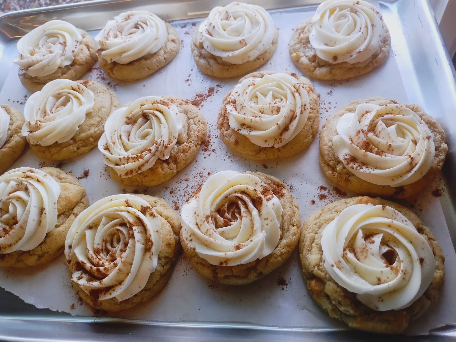 Cookies topped with buttercream frosting shaped like roses, dusted with cinnamon, on a tray.