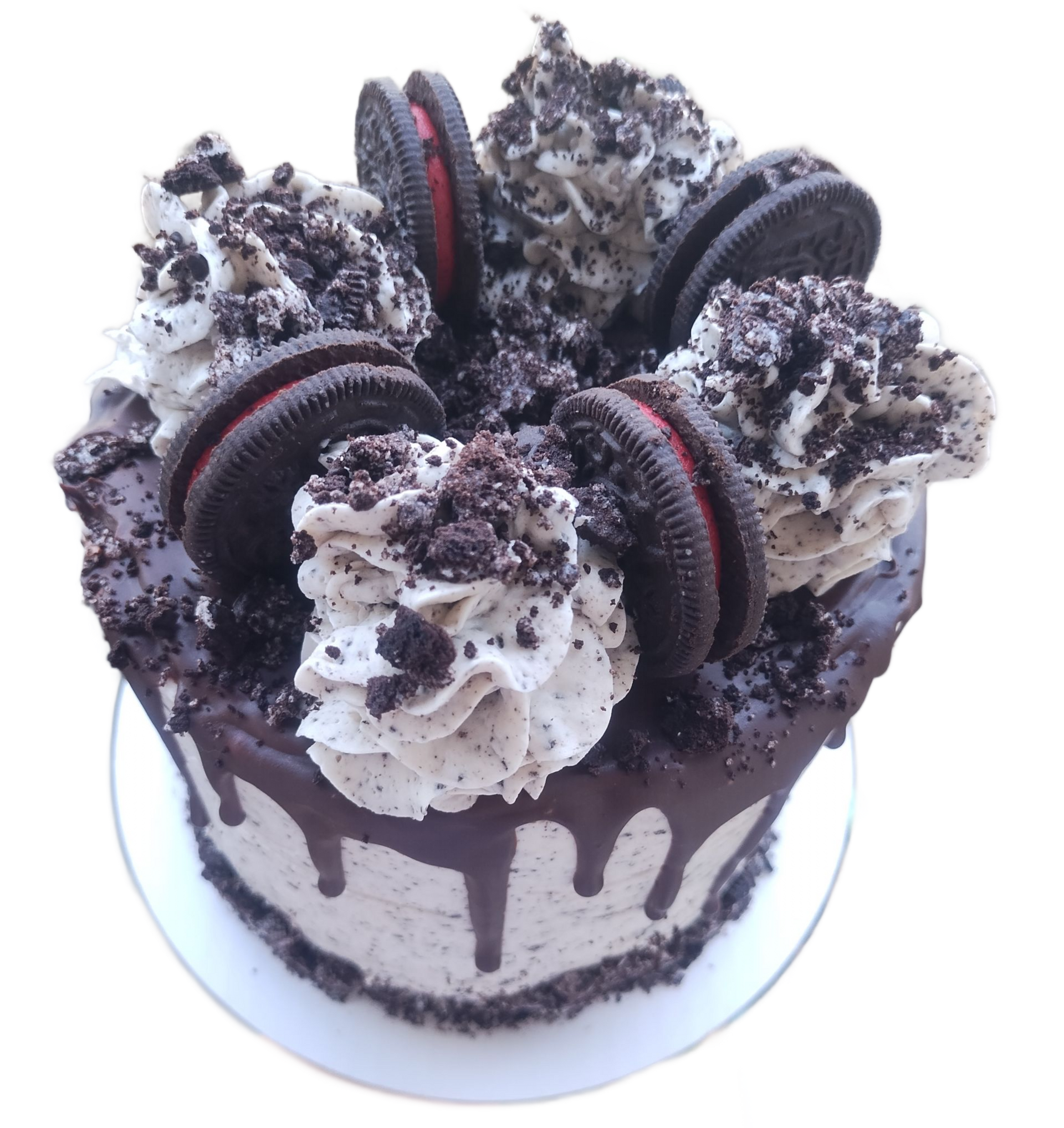Oreo cake with whipped cream, dripping chocolate, and crushed cookie crumbs on a white plate.