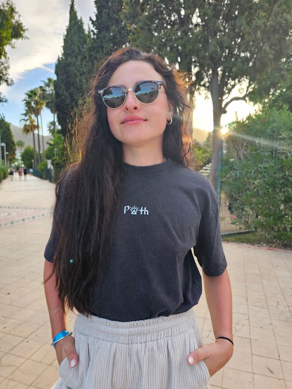 A woman wearing sunglasses and a black t-shirt is standing on a sidewalk.