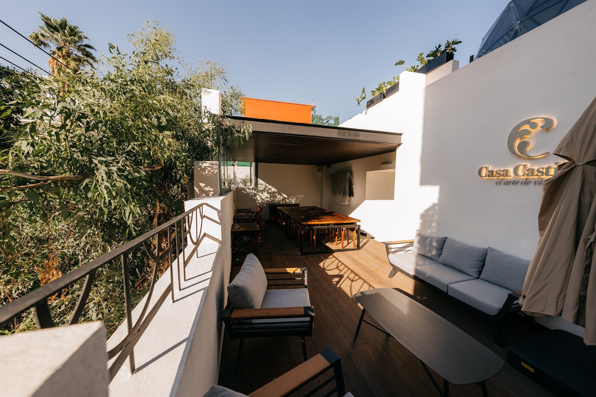 A balcony with a couch , table , chairs and umbrellas.