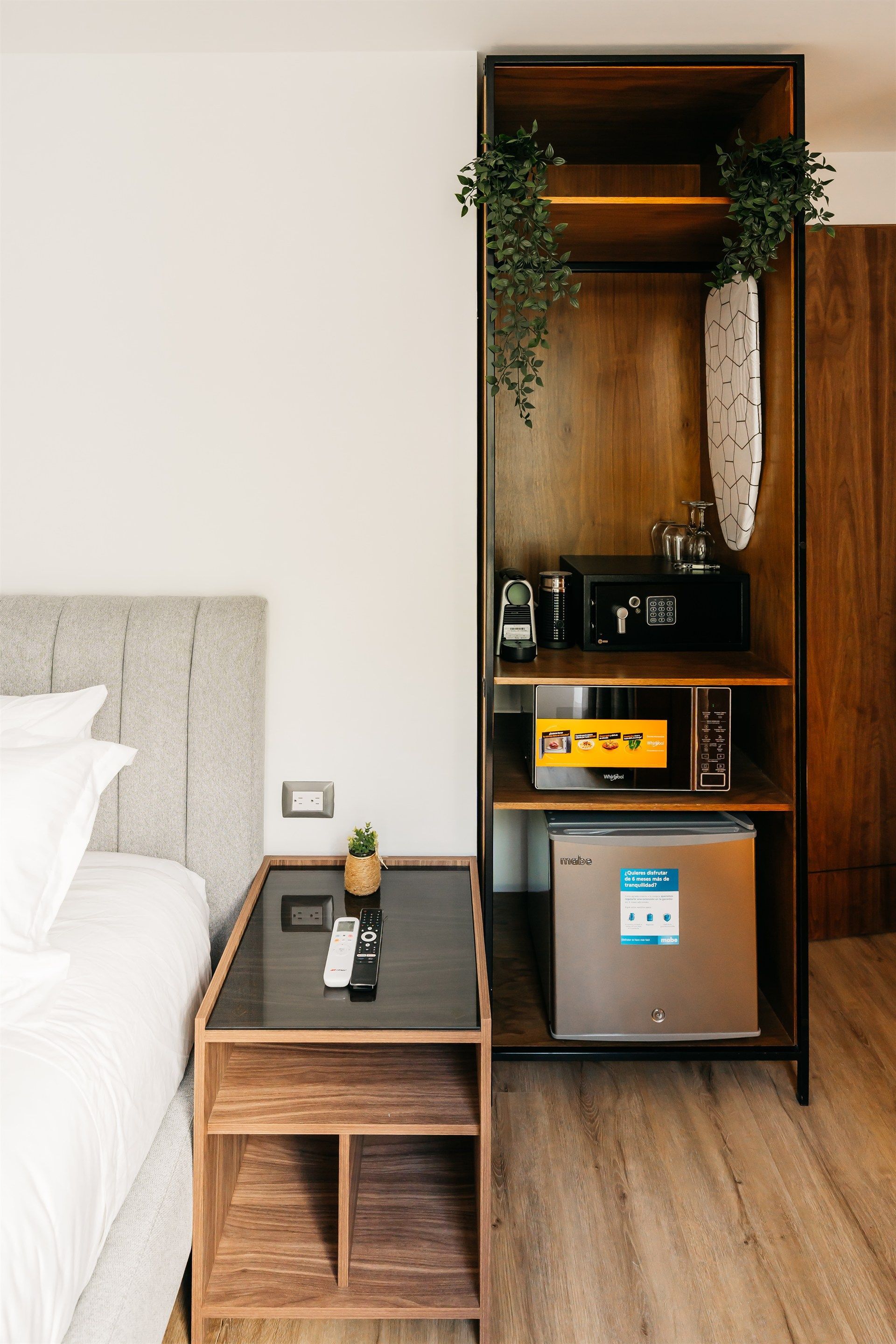 Una habitación de hotel con una cama, una mesita de noche, una nevera, un microondas y una caja fuerte.