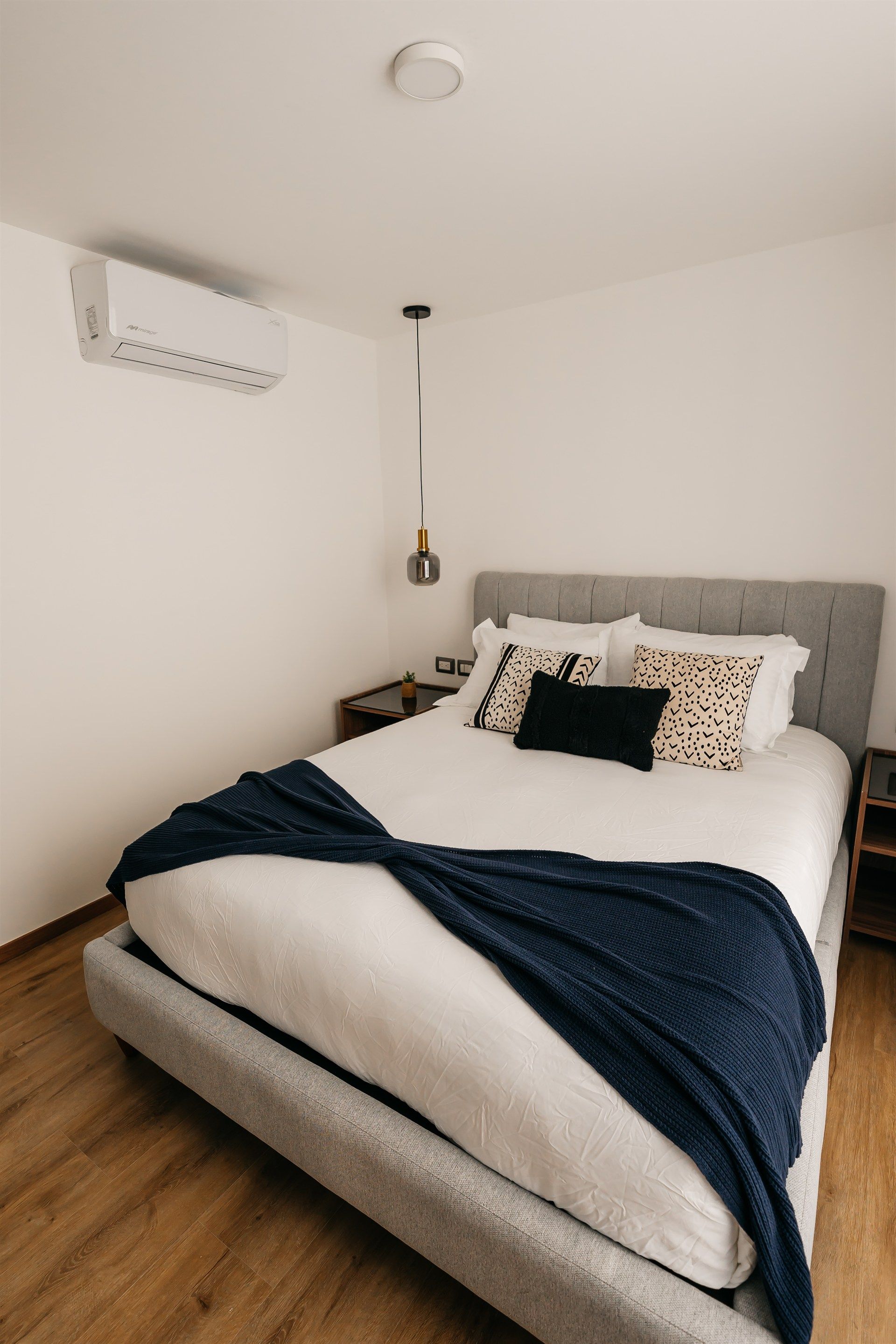 Un dormitorio con una cama, mesita de noche y aire acondicionado.