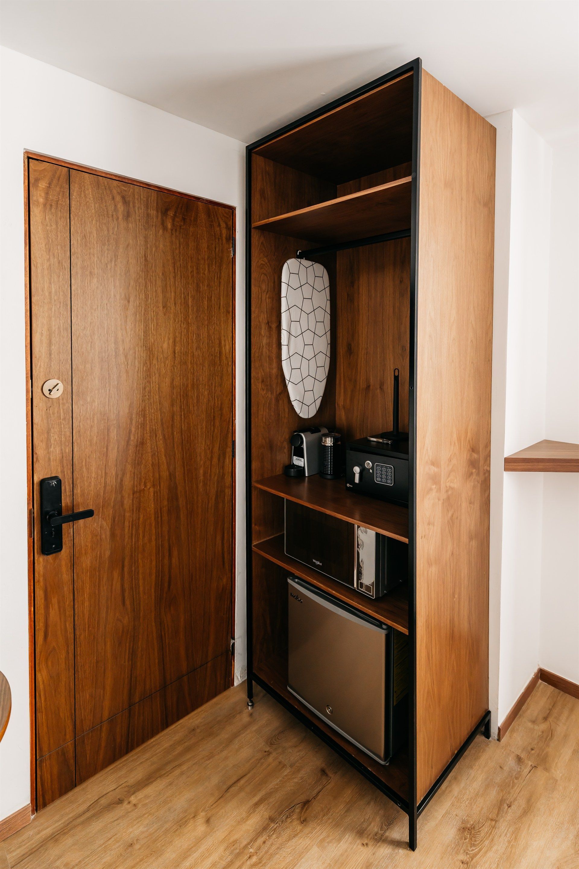 Una habitación de hotel con una puerta de madera, un estante de madera y un pequeño refrigerador.