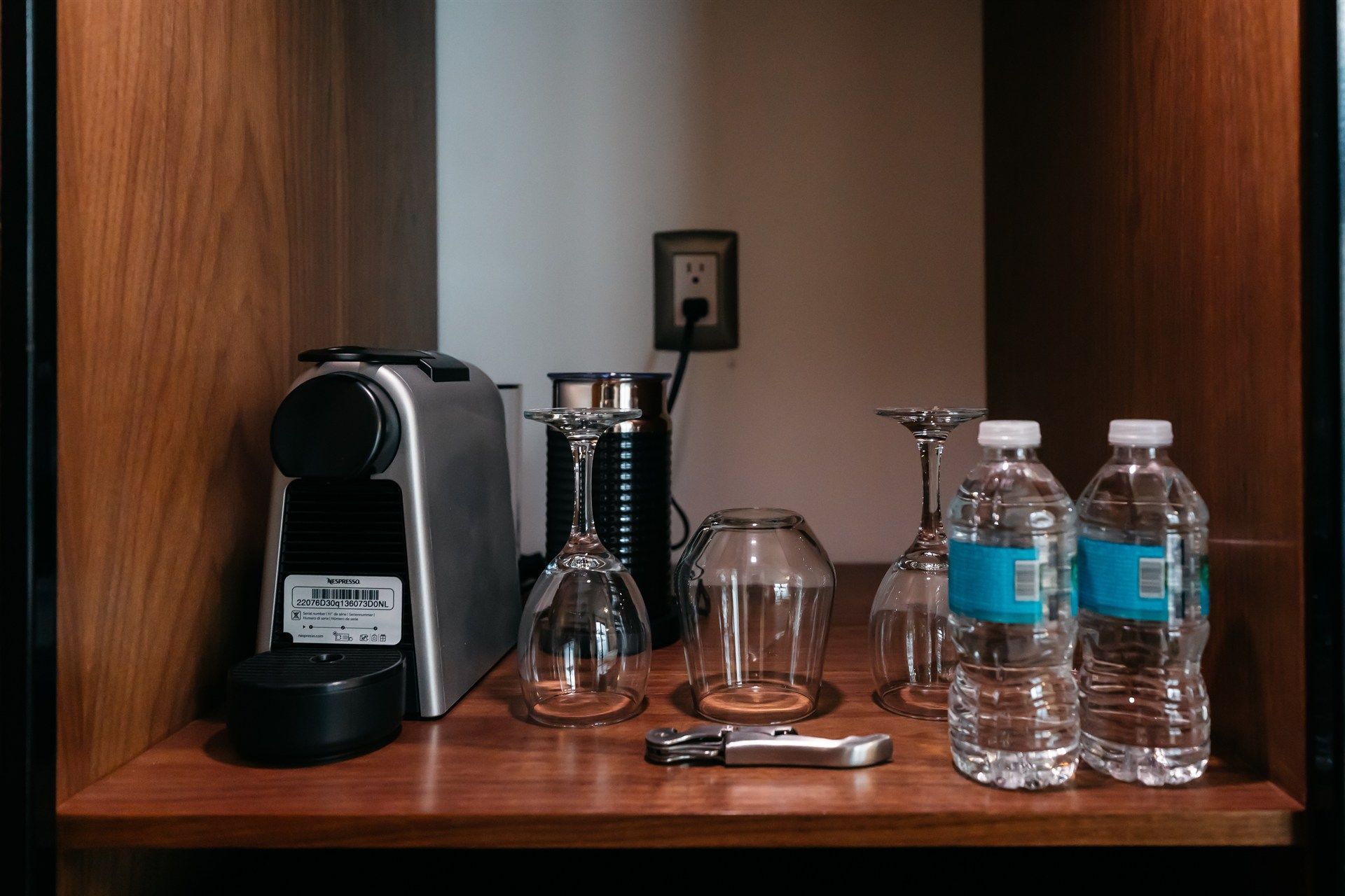 Un estante con botellas de agua, copas de vino y una cafetera.
