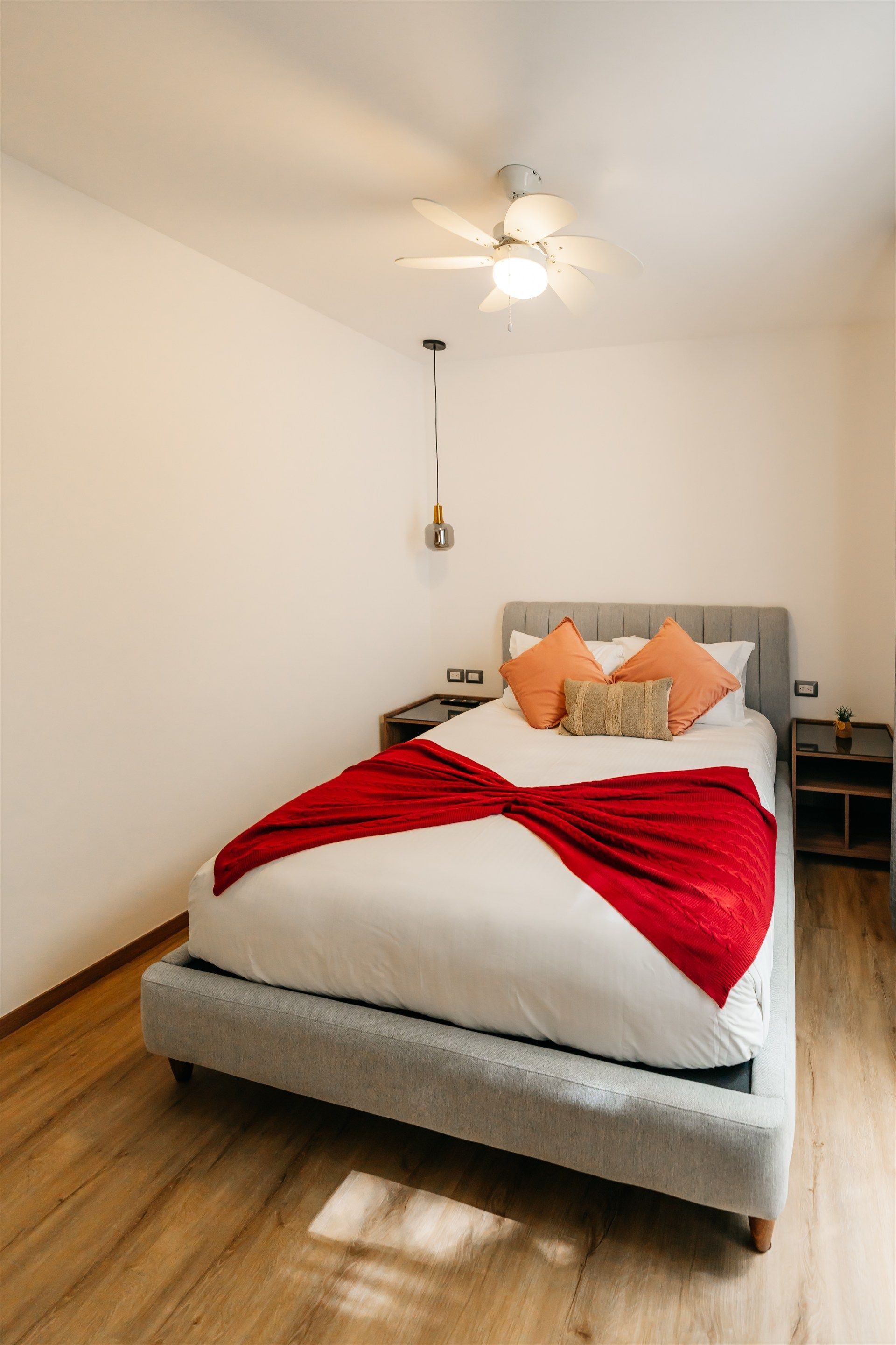Una cama con una manta roja y almohadas en un dormitorio con ventilador de techo.