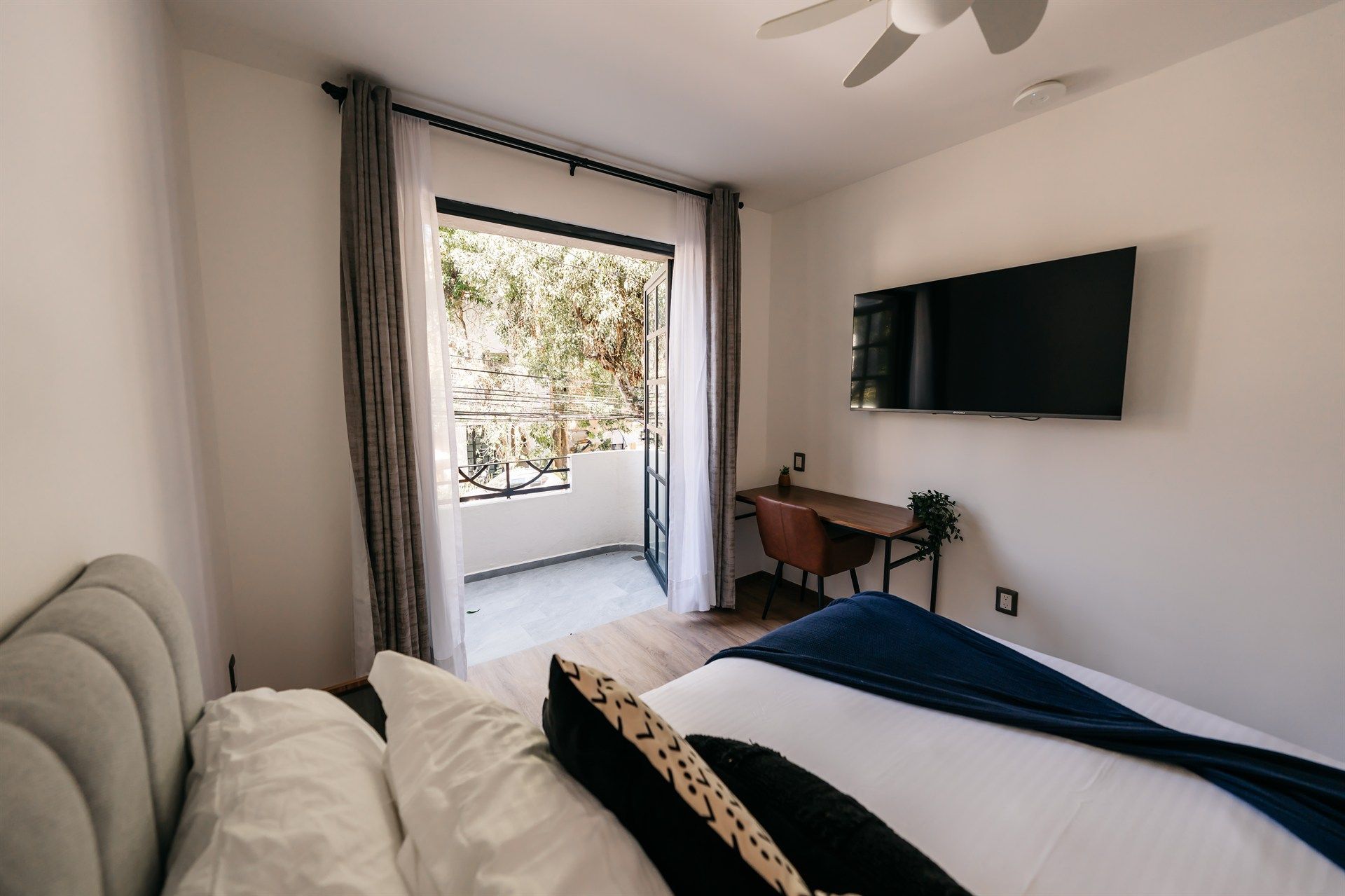 Un dormitorio con cama, escritorio, televisión y balcón.