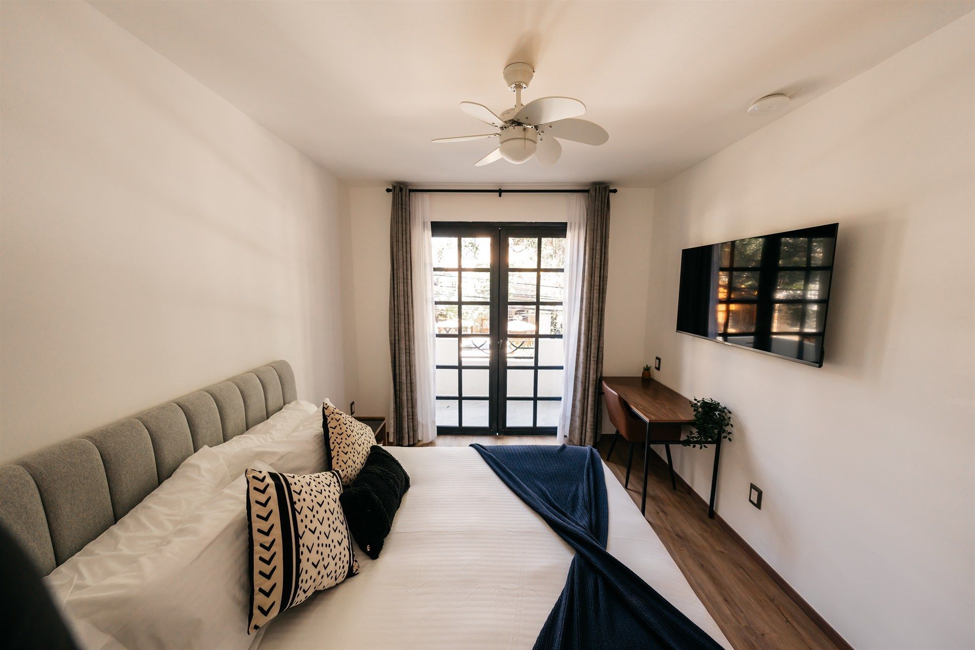 Un dormitorio con una cama, escritorio, televisión y ventilador de techo.