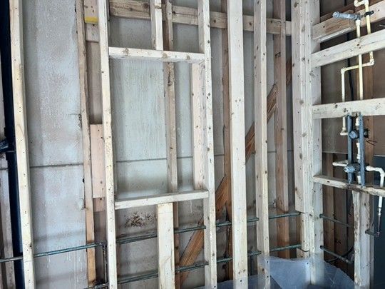 Wooden wall framing, with plumbing pipes visible, in a construction setting.