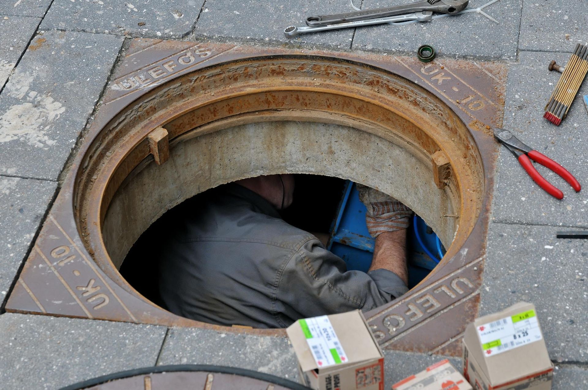 A man is working on a manhole cover on the sidewalk
