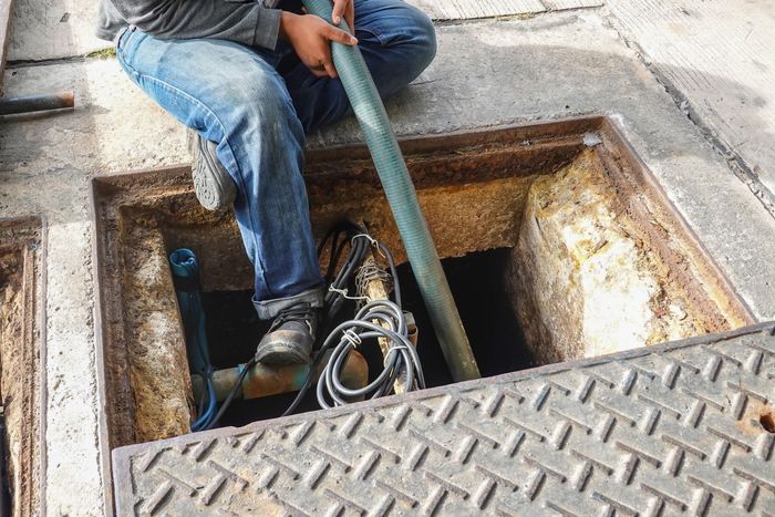 A man is sitting in a manhole cover holding a hose.