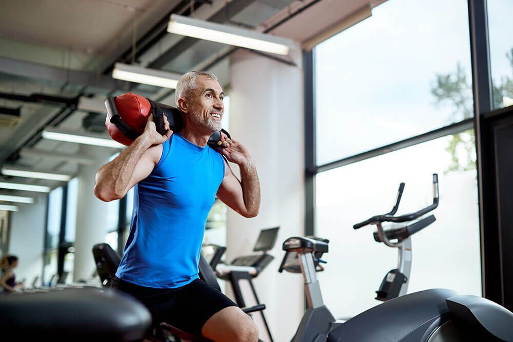 A man is lifting a medicine ball on his shoulders in a gym.