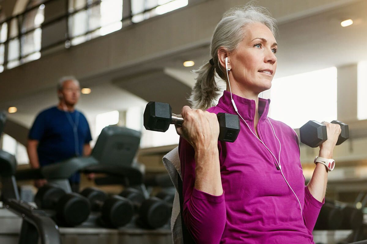 An older woman is lifting dumbbells in a gym.