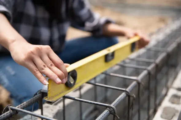 Person leveling rebar with a yellow spirit level at a construction site