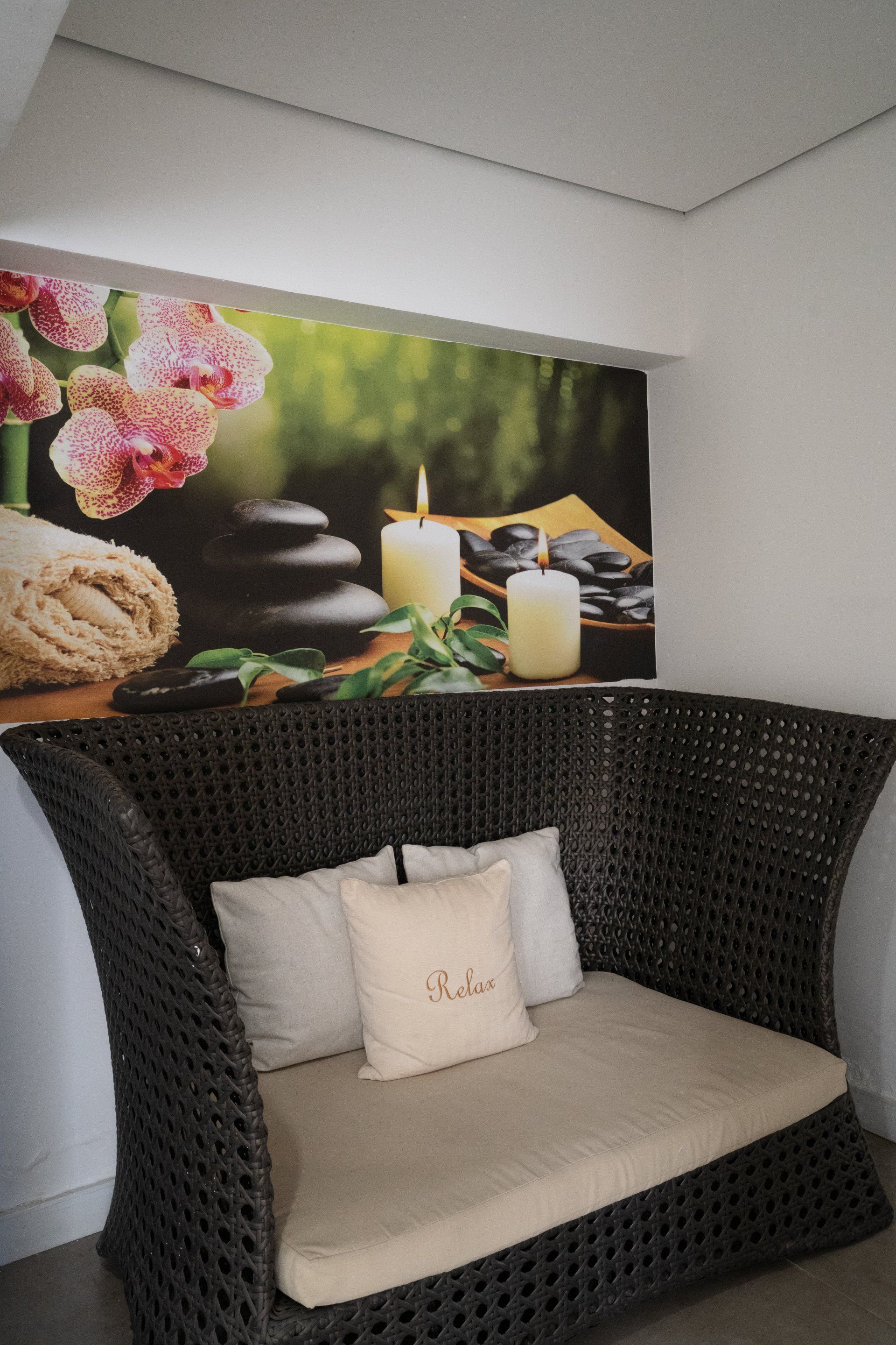 Bancos de vime em frente a um mural com tema de spa, decorado com velas, pedras e orquídeas.
