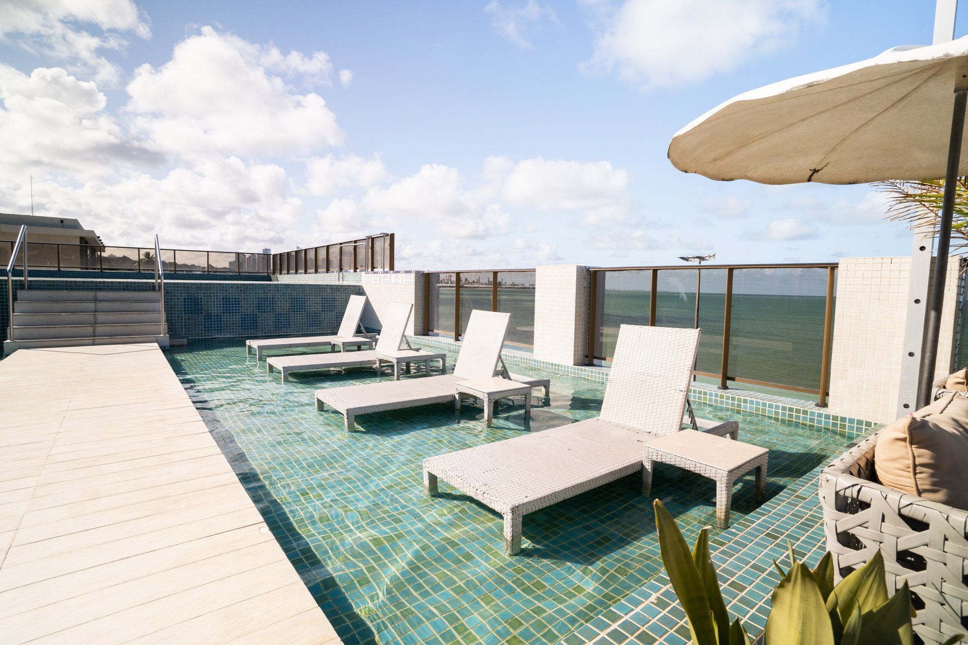 Piscina na cobertura com espreguiçadeiras, guarda-sol e vista para o céu em um dia ensolarado.