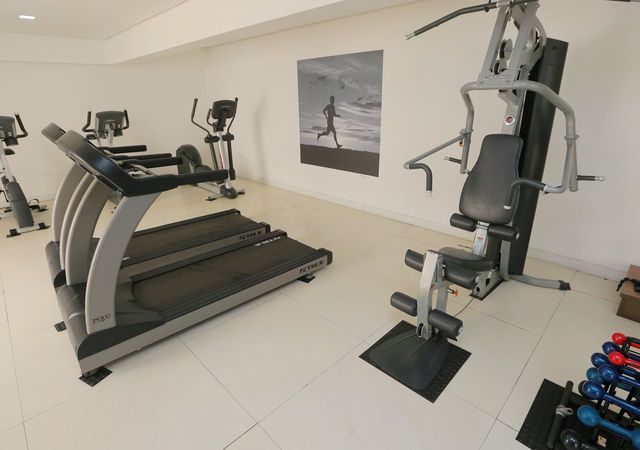 Academia com esteira, elíptico, aparelho multifuncional, suporte para pesos e um pôster de corredor.