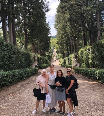 A group of women standing on a gravel road lined with trees A group of women standing on a gravel road lined with trees