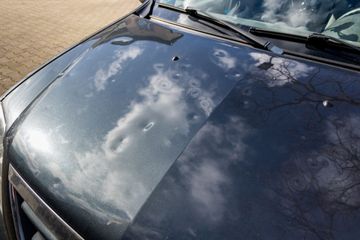A close up of a car 's hood with clouds reflected in it.