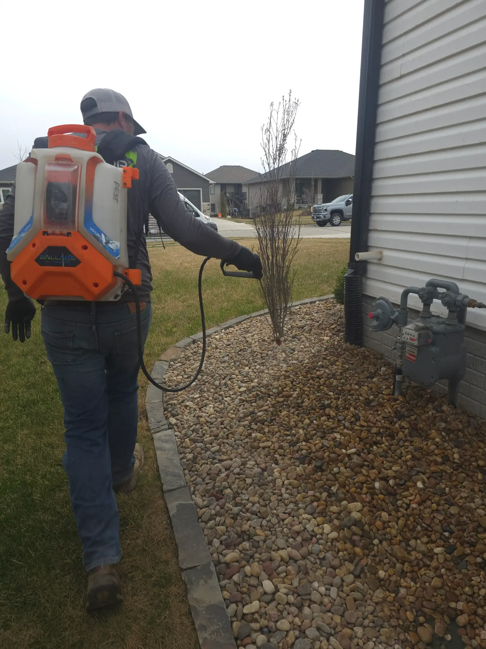 A man is spraying a house with a backpack sprayer.