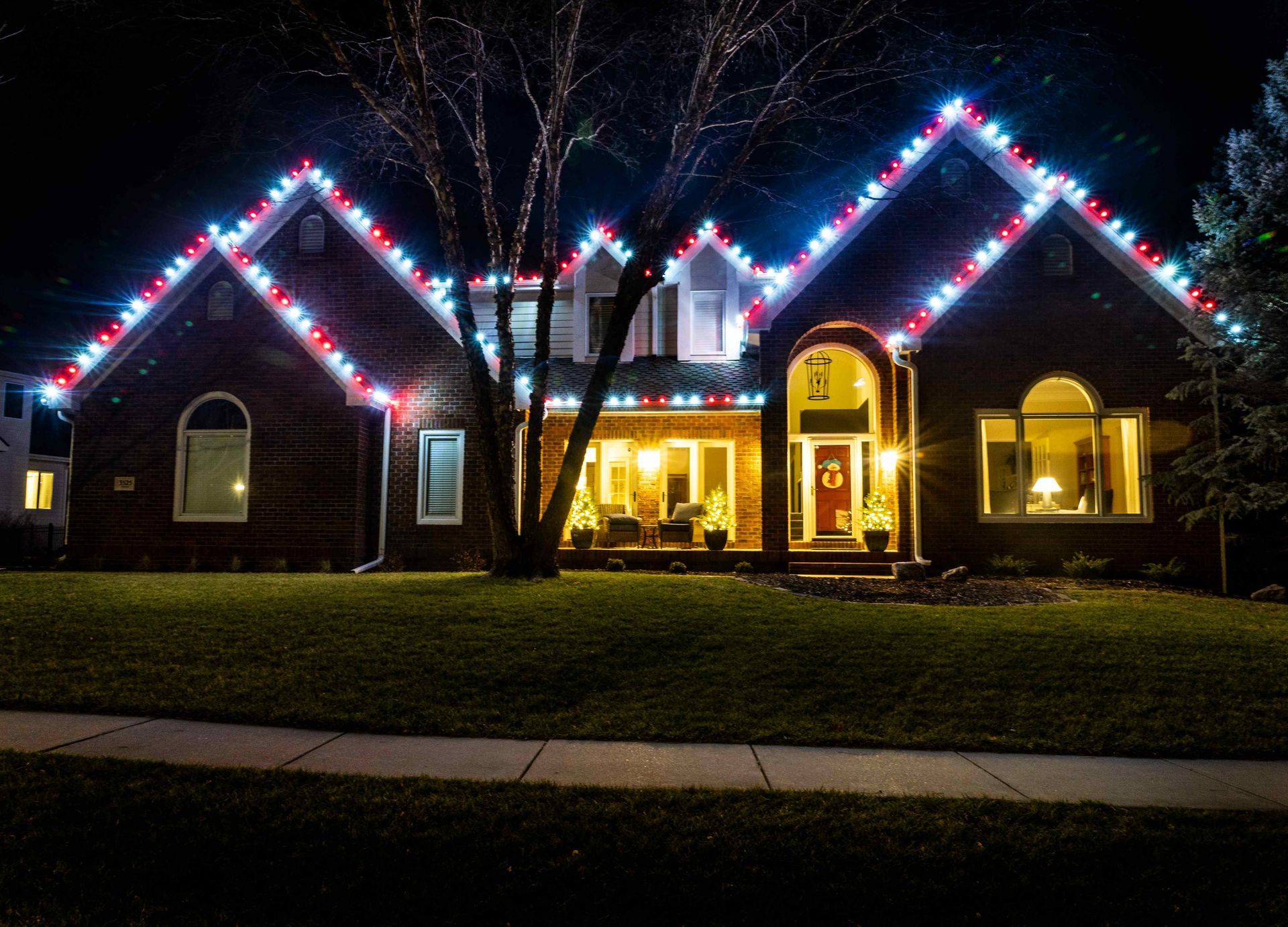 House with red, white, and blue lights along the roofline at night.