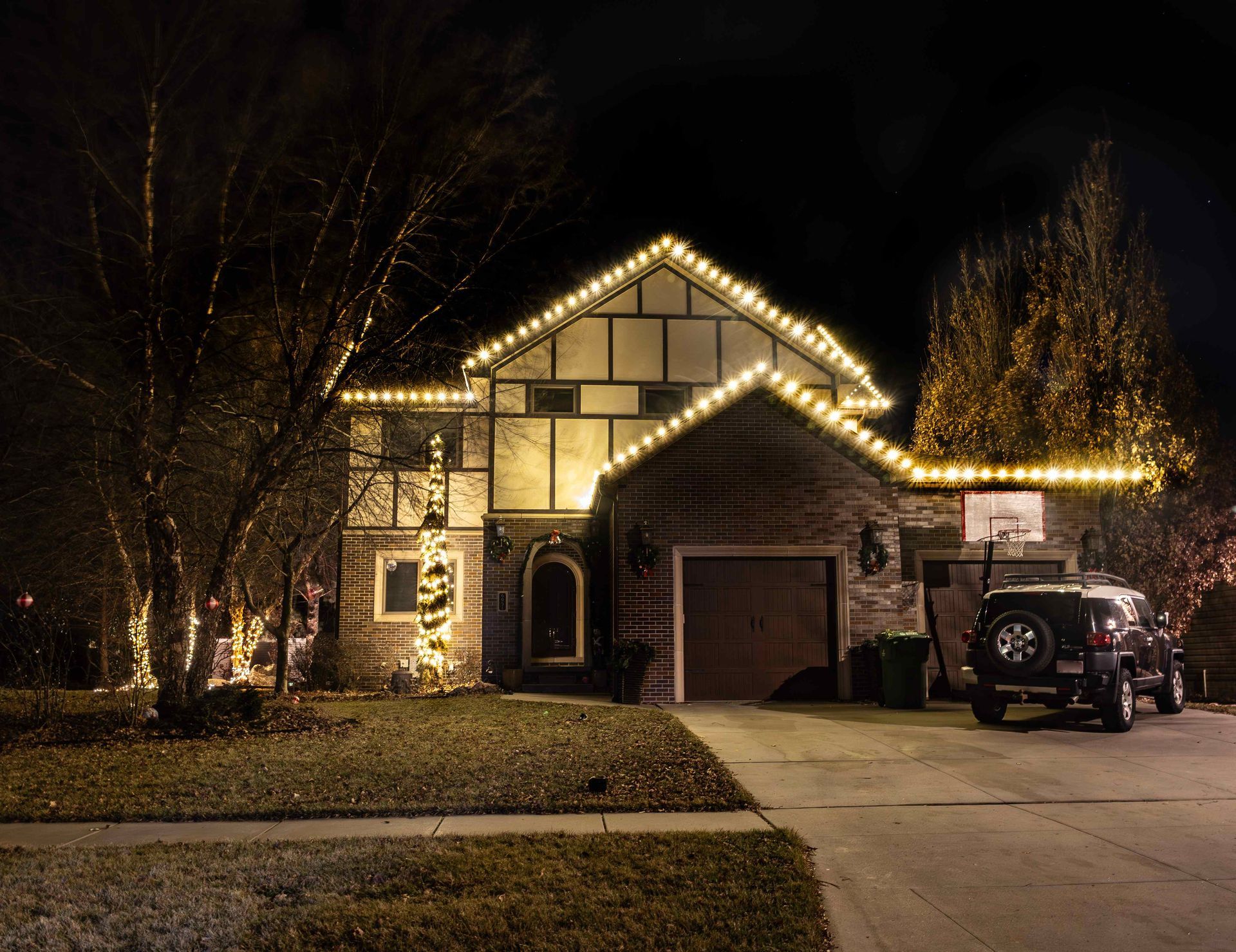 House decorated with white Christmas lights at night, with a car in the driveway.