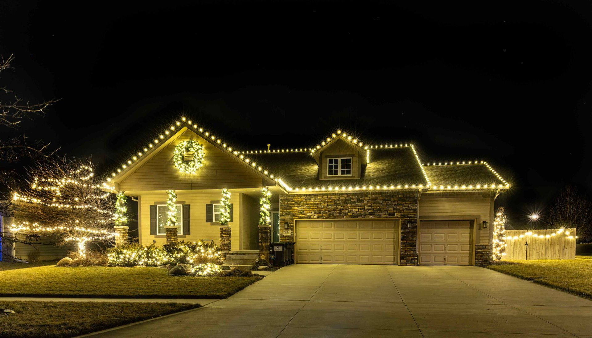 House decorated with Christmas lights at night; golden lights outline the roof and a Christmas tree in front.