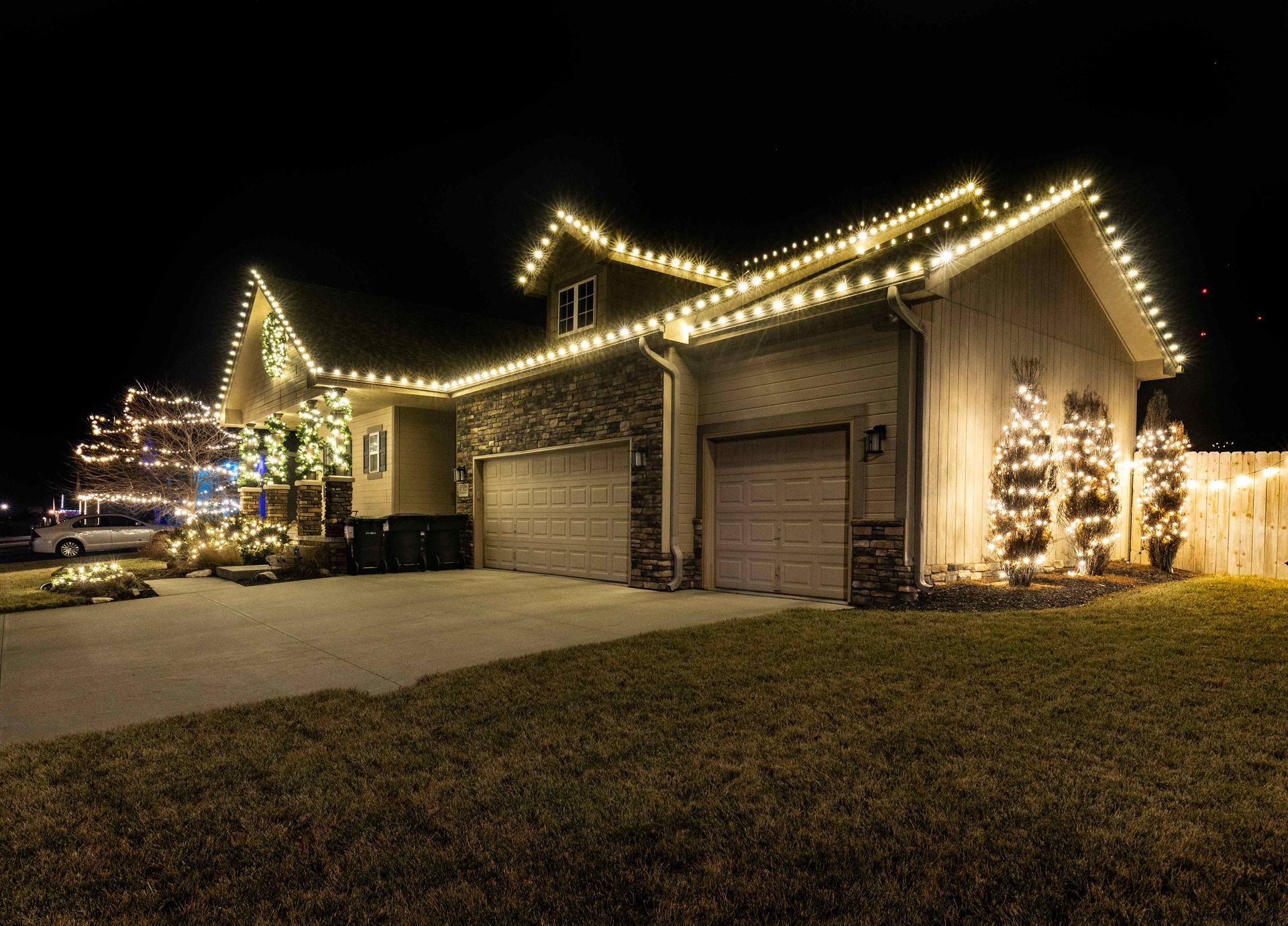 House with Christmas lights decorating roof, porch, and trees at night.