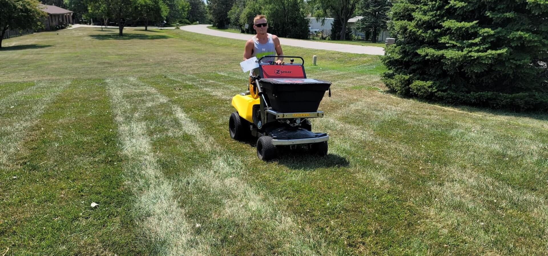 A man is riding a yellow lawn mower on a lush green lawn.