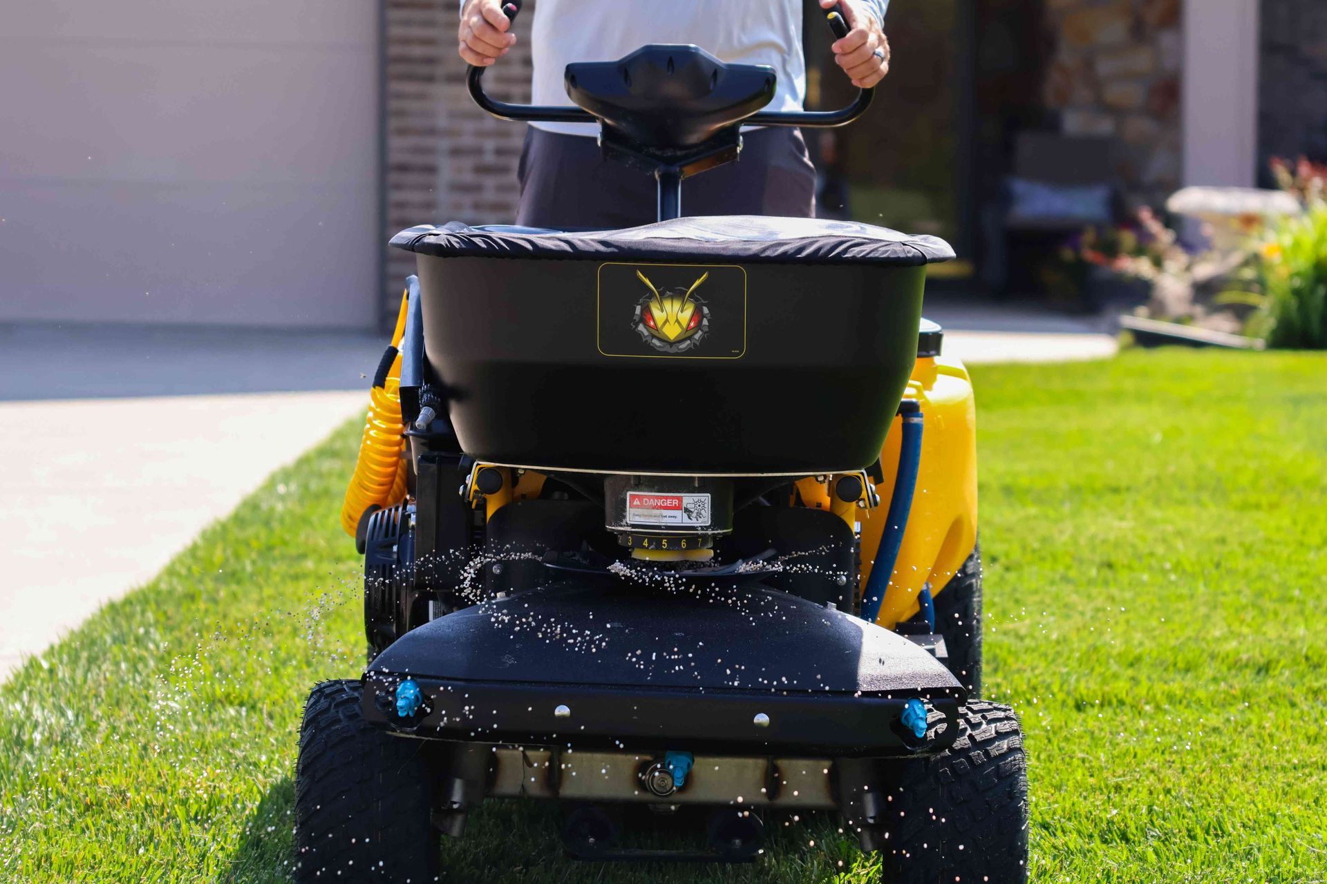 A man is riding a lawn mower with a spreader attached to it.