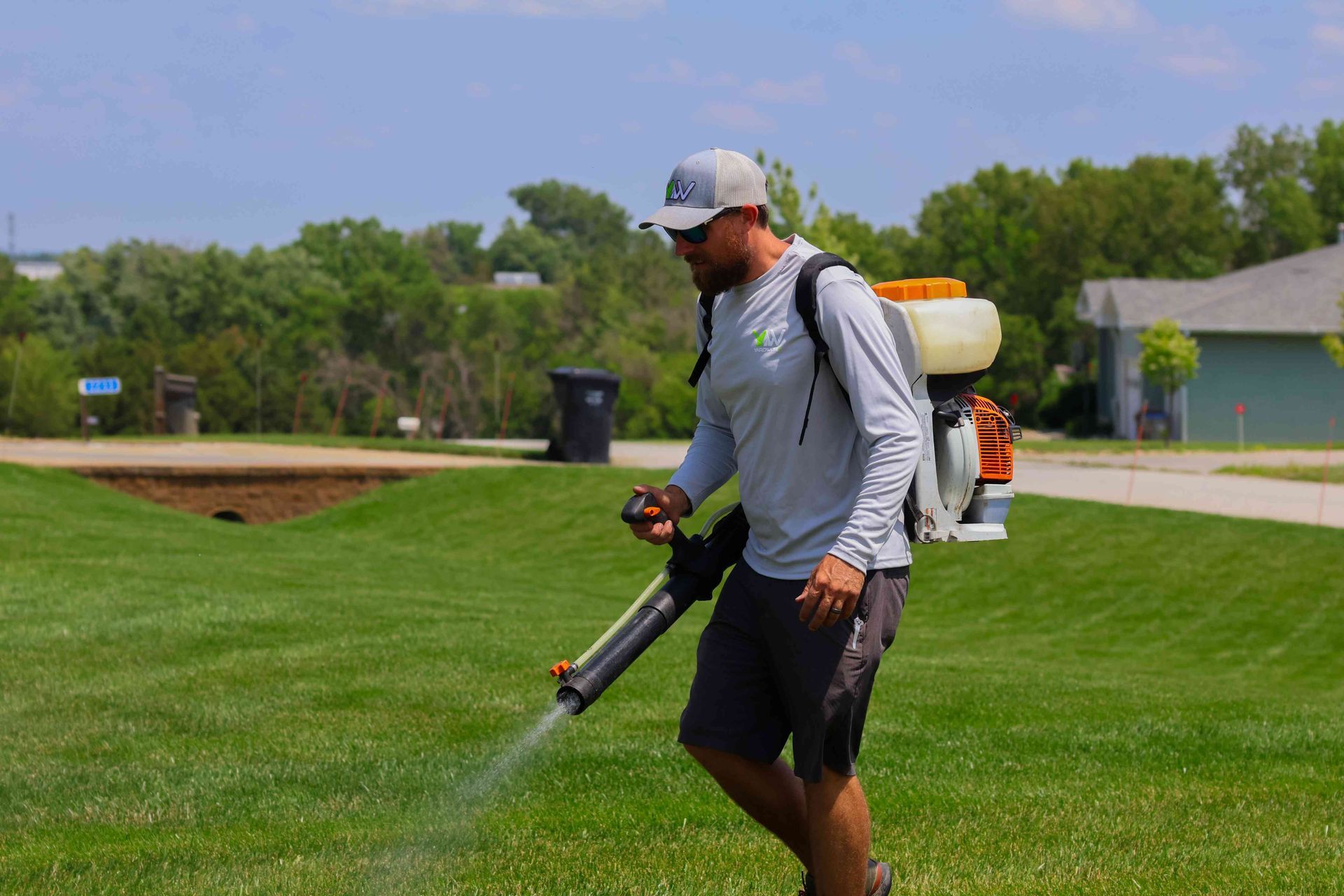 A man is spraying a lawn with a backpack sprayer.