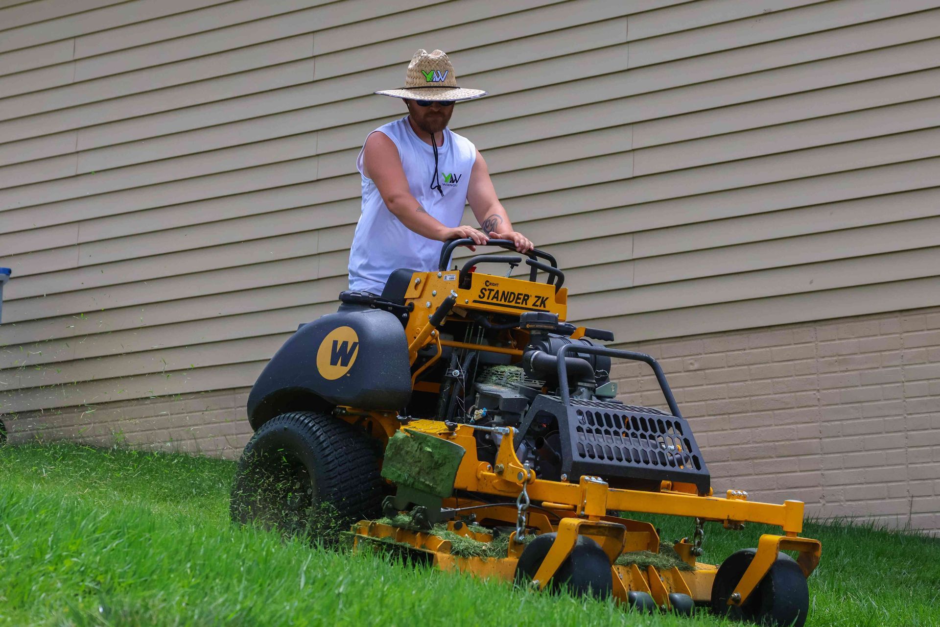 A man wearing a hat is riding a yellow lawn mower