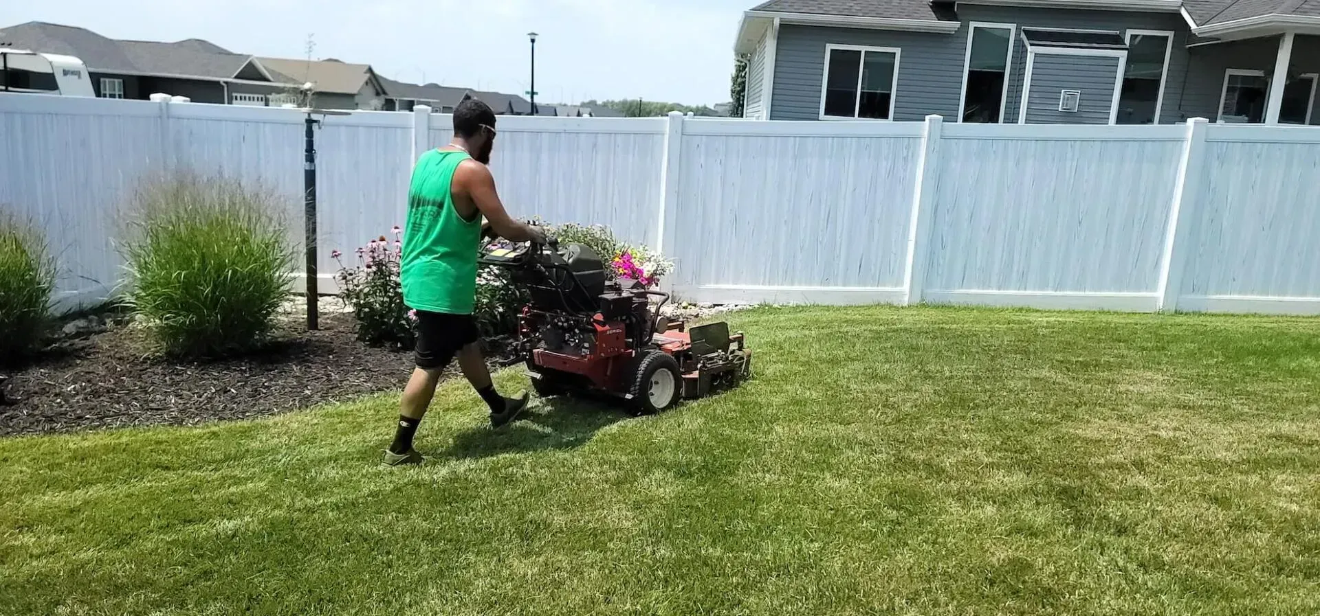 A man is mowing a lush green lawn with a lawn mower.