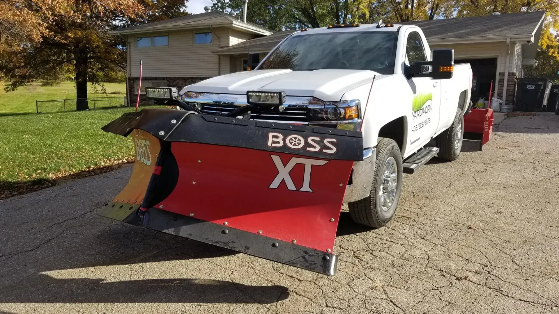 A white truck with a red plow on the front is parked in front of a house.