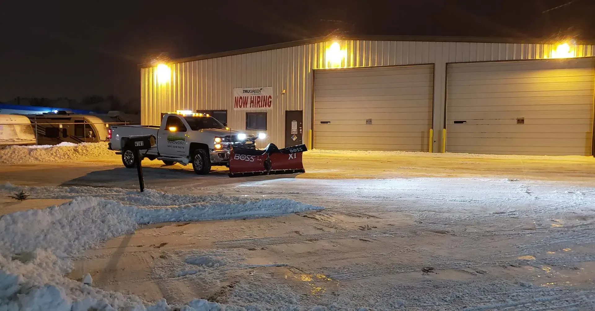A snow plow is parked in front of a building at night.